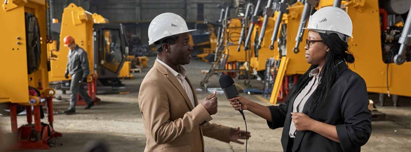 Two people conducting an interview within a manufacturing plant. 